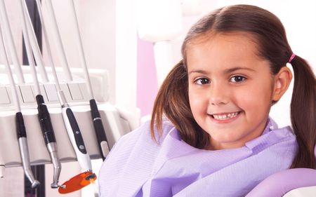 a little girl is sitting in a dental chair and smiling