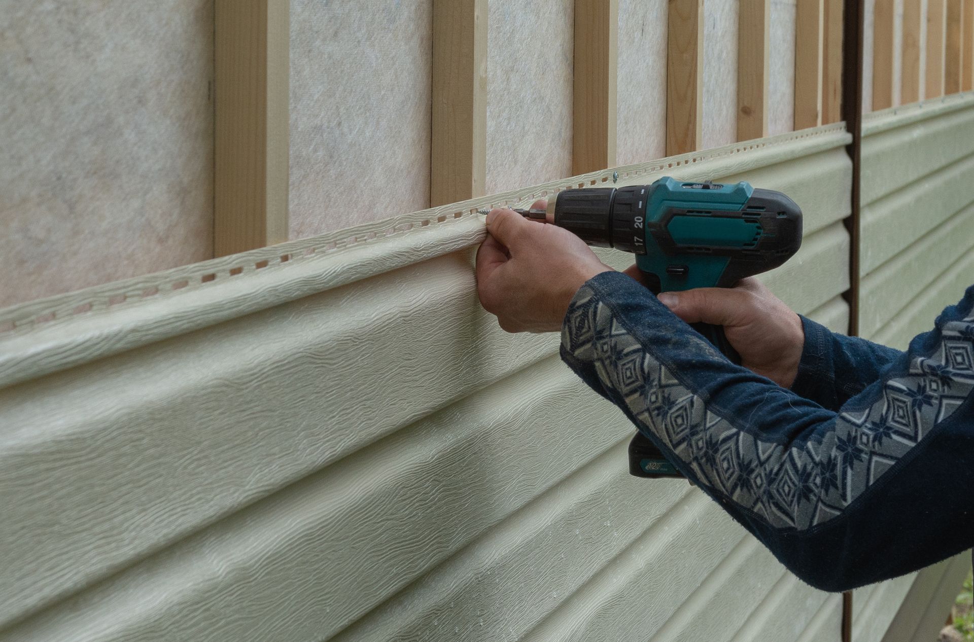 person screwing new siding onto their house for siding installation 