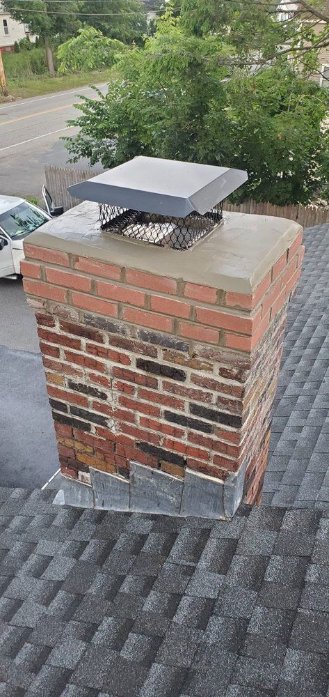 Brick chimney with a metal cap, on a gray shingle roof.