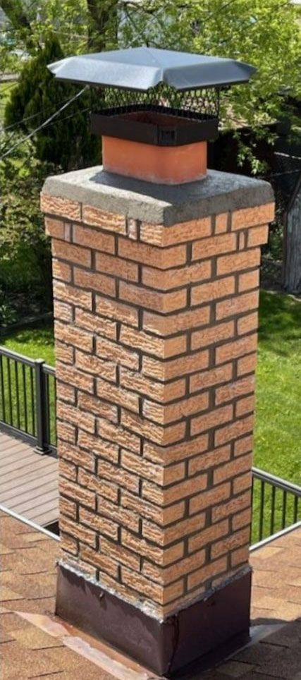 Brick chimney with a metal cap on a rooftop.