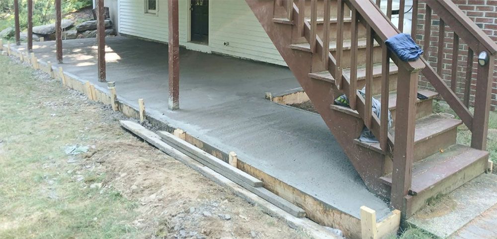 Newly poured concrete patio with wooden stairs and supports.