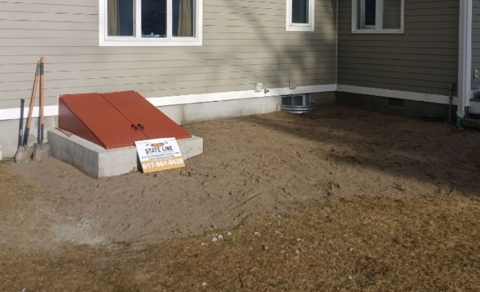 A red storm shelter door sits on a concrete pad in front of a light brown house.