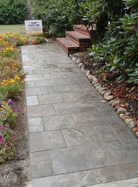 A gray stone pathway leads to brick steps, flanked by flower beds and shrubs.