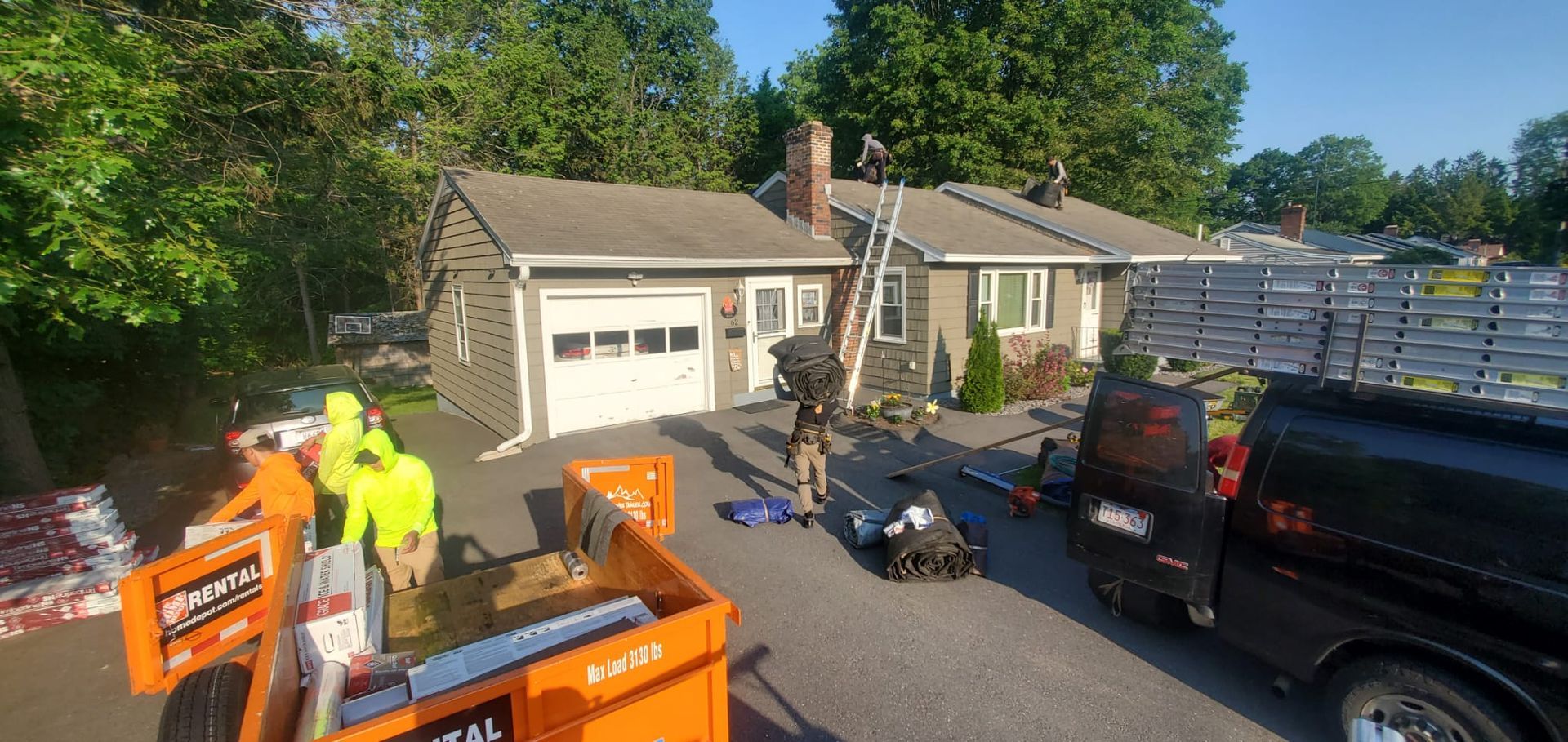Roofers working on a house, with materials and equipment visible.