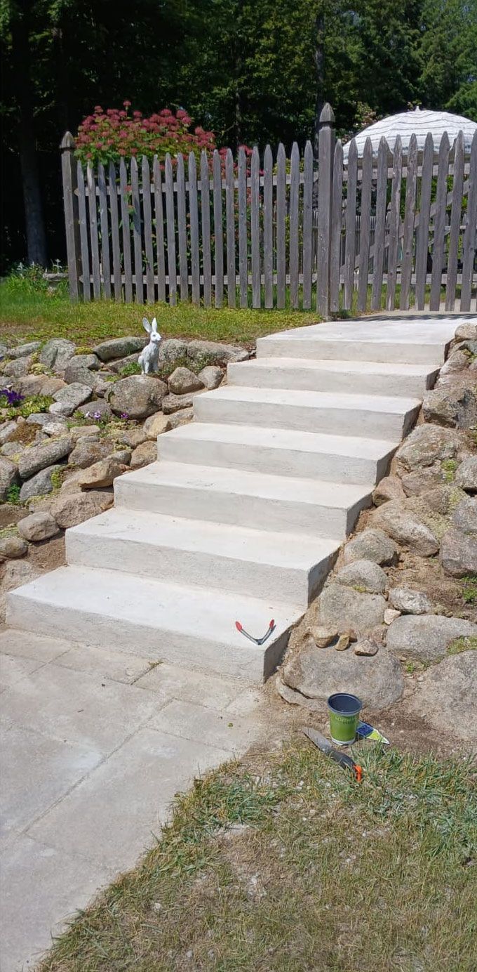 Concrete steps leading up to a wooden fence and gate in a yard. A garden with rocks and grass.