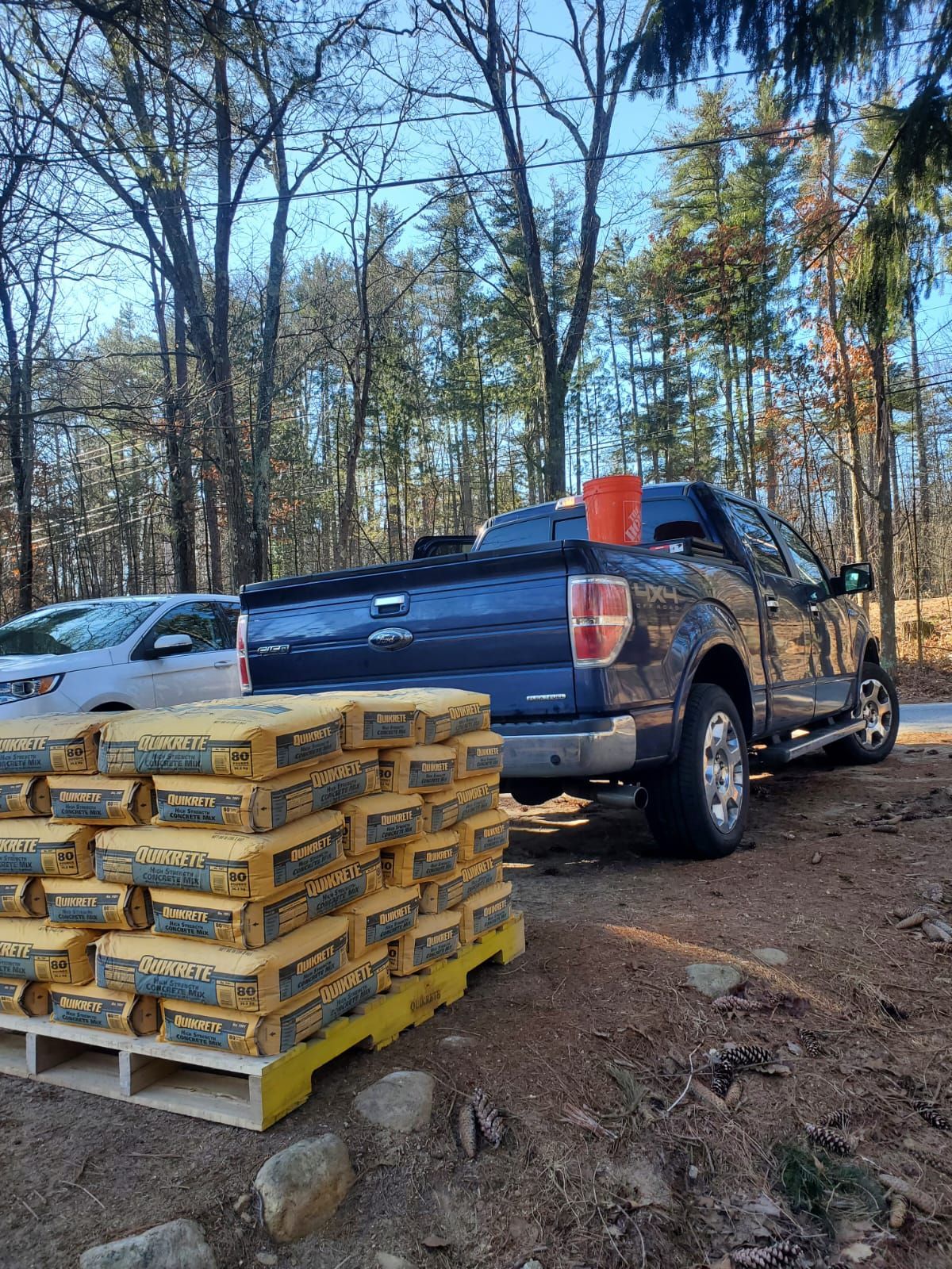 Blue truck parked near a pallet of cement bags in a wooded area.