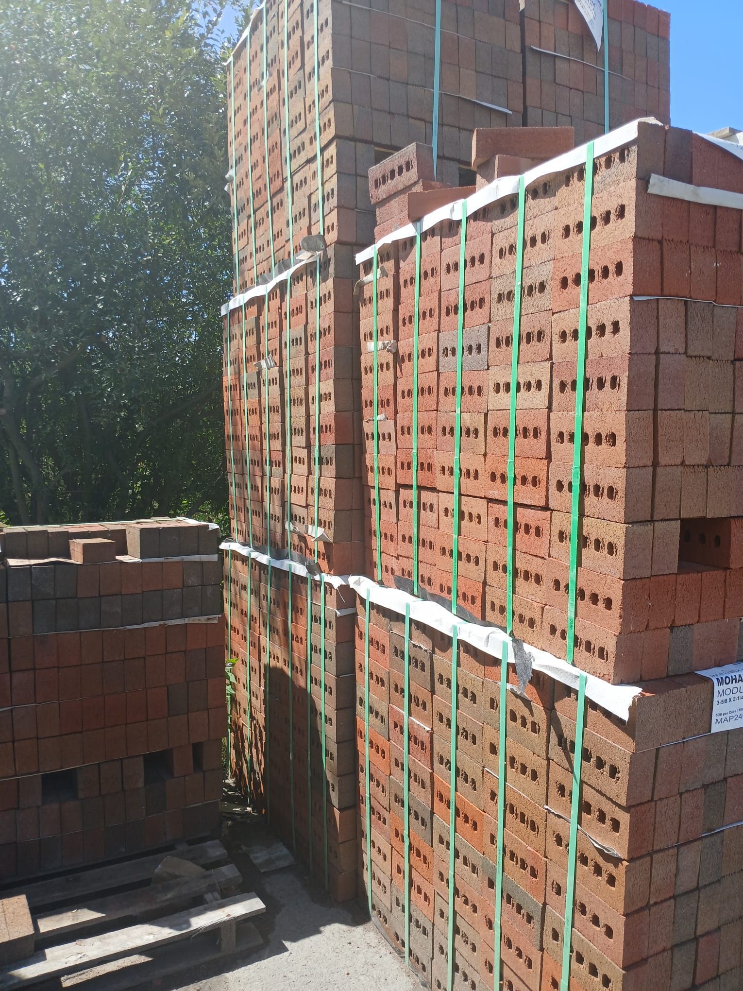 Stacks of red bricks bound with green straps, outdoors.