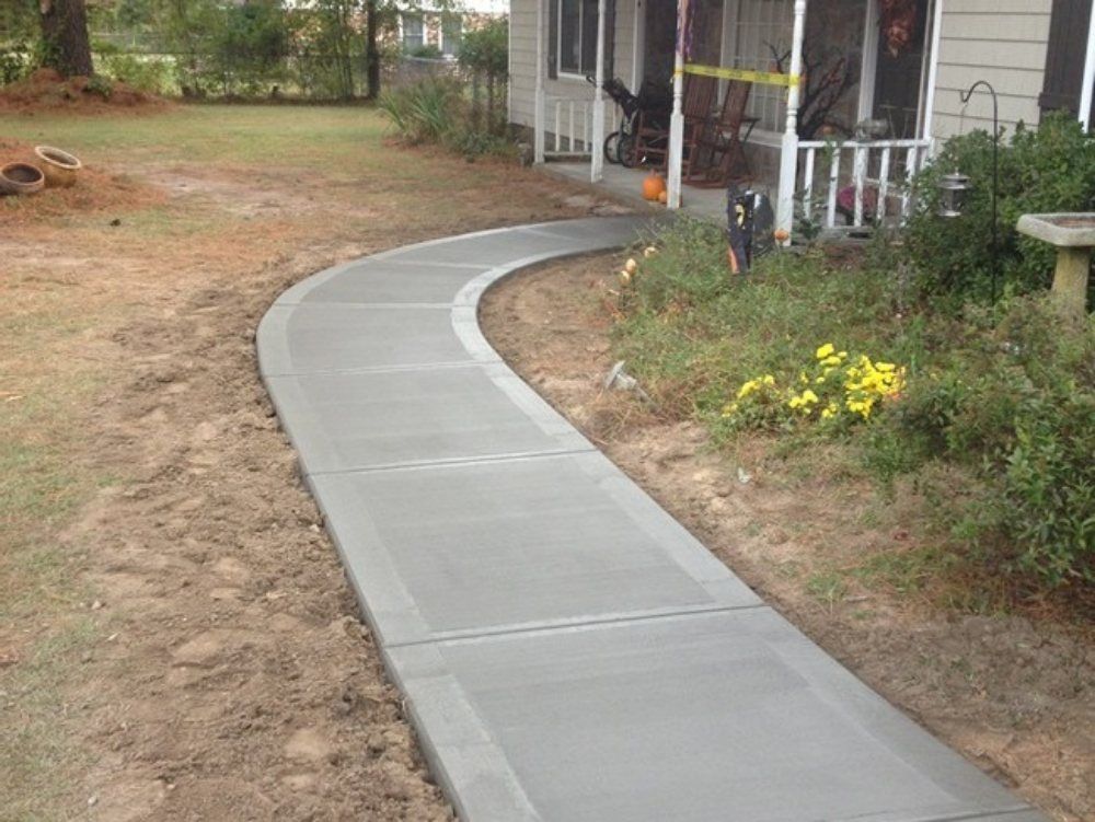 New concrete walkway curves toward a house with a screened porch; brown soil on either side.