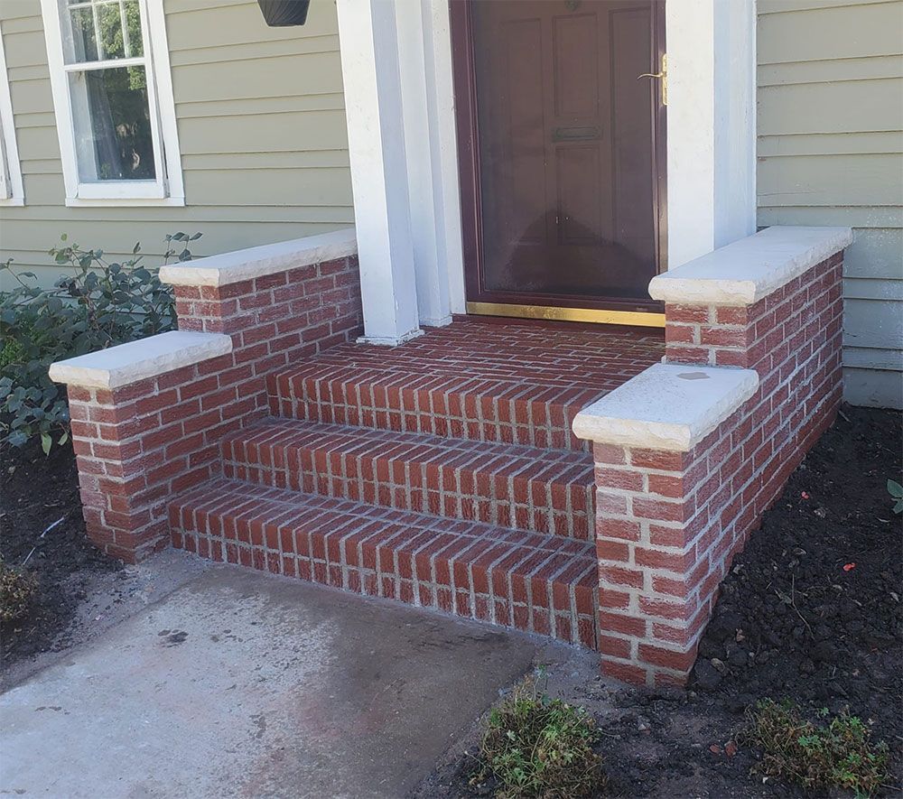 Brick steps leading up to a brown door, with stone caps, on a green house exterior.