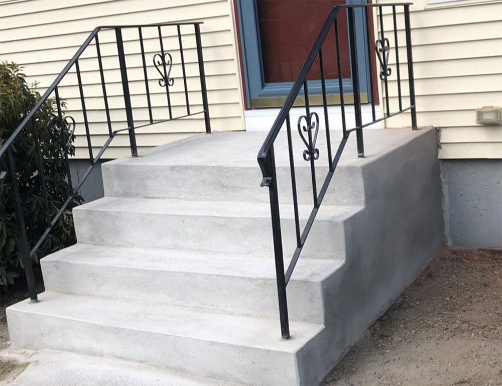 Concrete steps with black iron handrails leading to a house entrance.