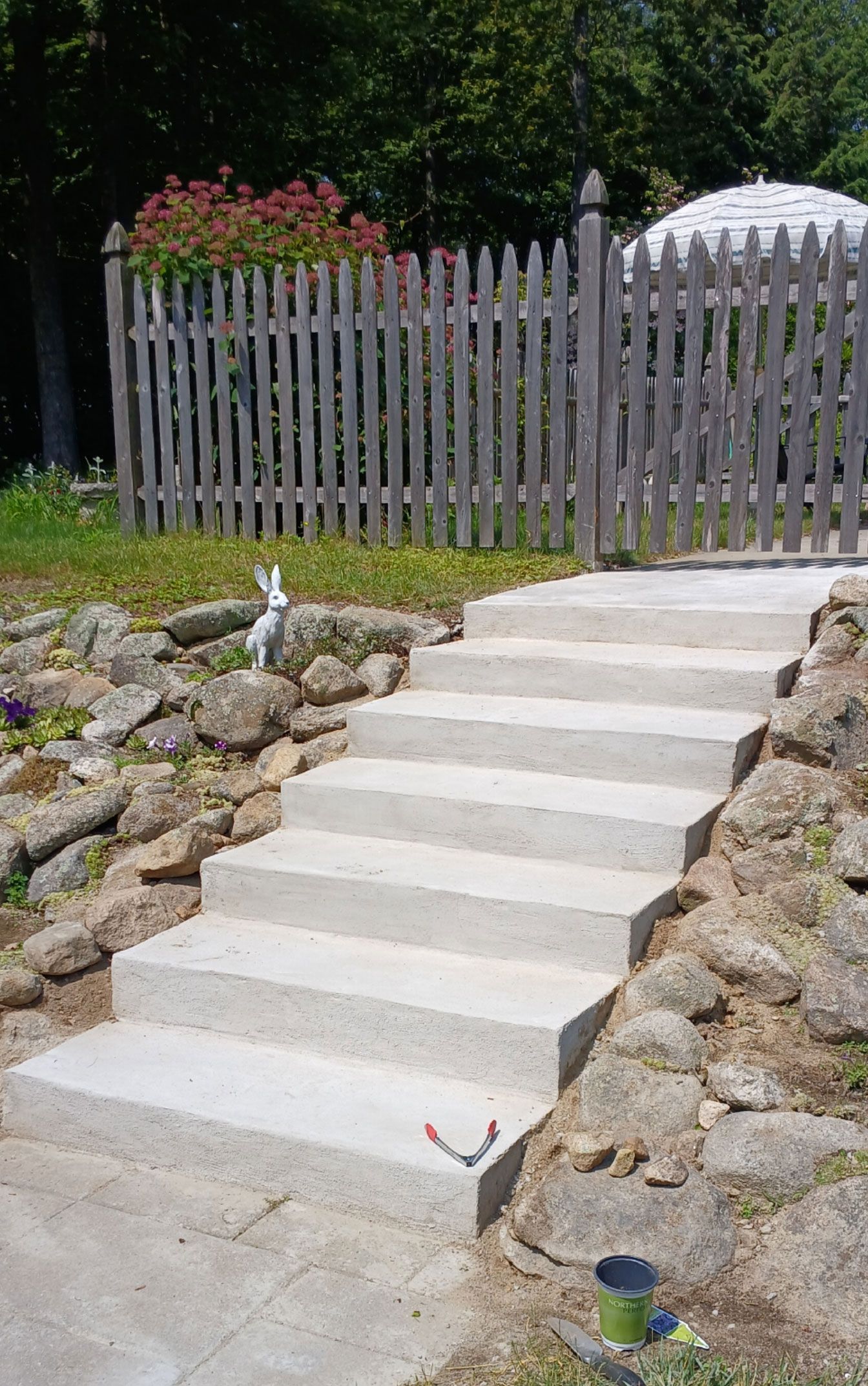 Concrete steps leading up to a picket fence and a small gazebo in a garden.