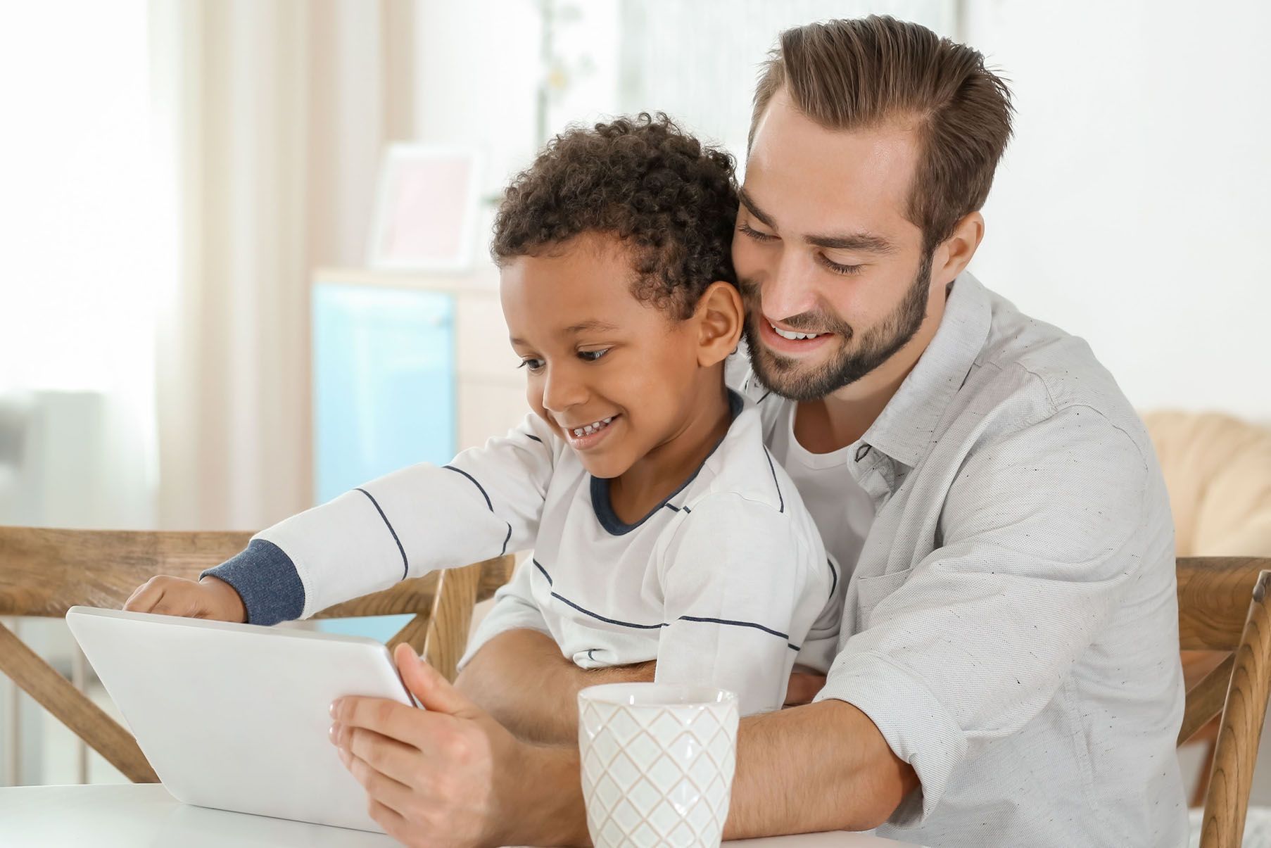 A man and a boy are sitting at a table looking at a tablet.