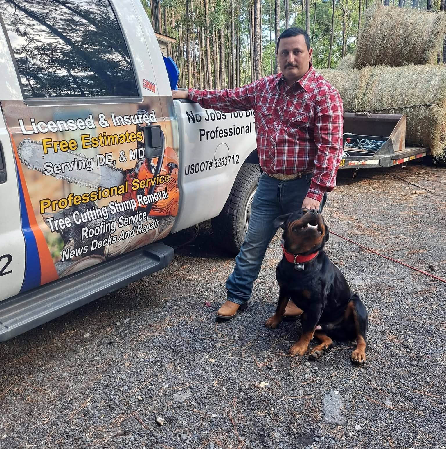 Man with Rottweiler dog stands by truck with tree service logos, hay bales in background.