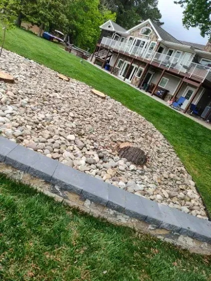 A rock garden with a gray border, next to green grass and a multi-story house.