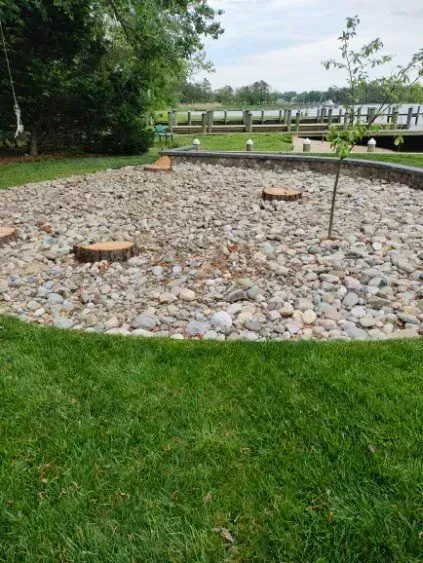 Gravel-filled garden bed with tree stumps, young tree, and lawn. Lake and dock in the background.