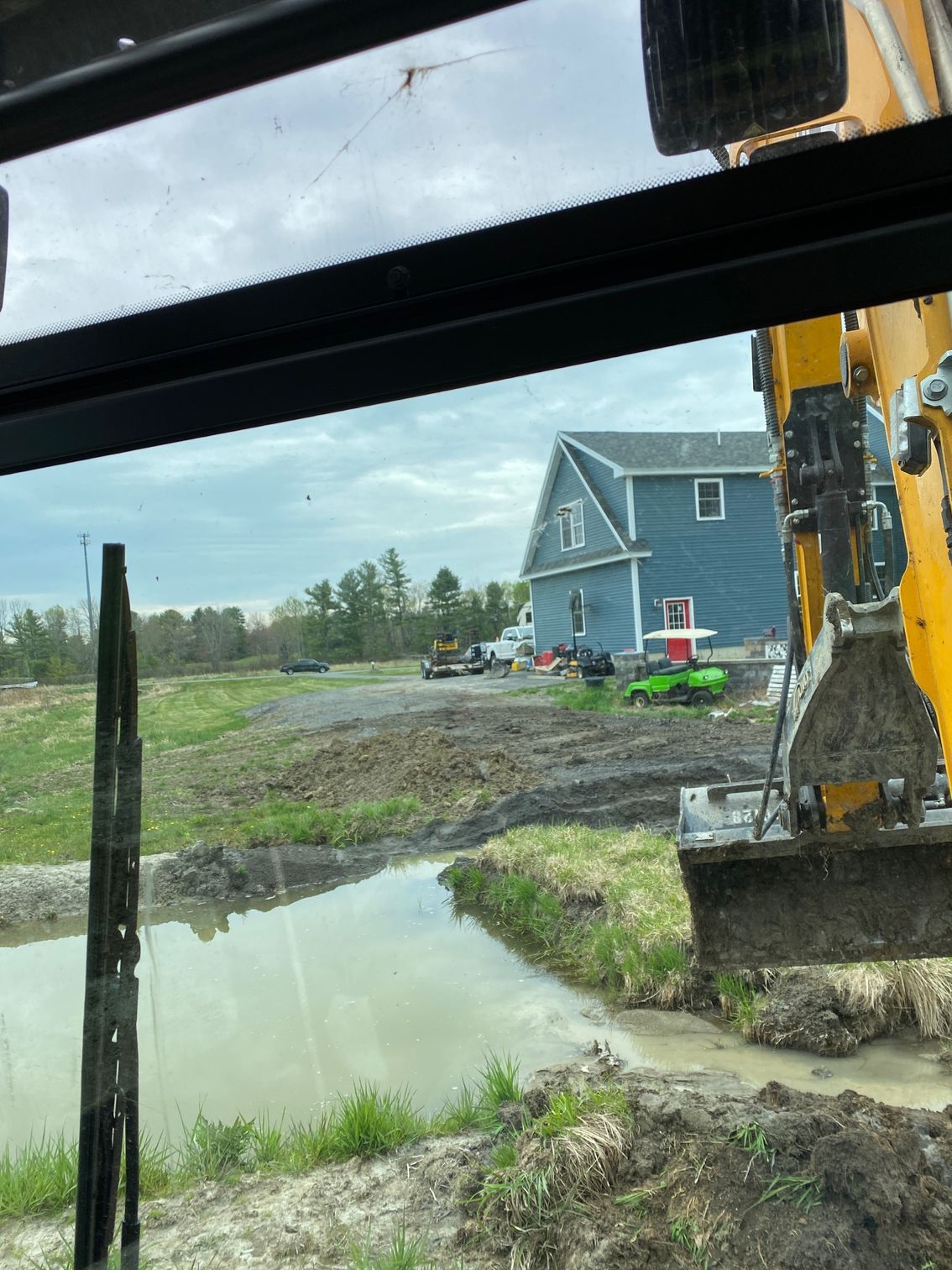 A yellow excavator is digging a hole in a field next to a house