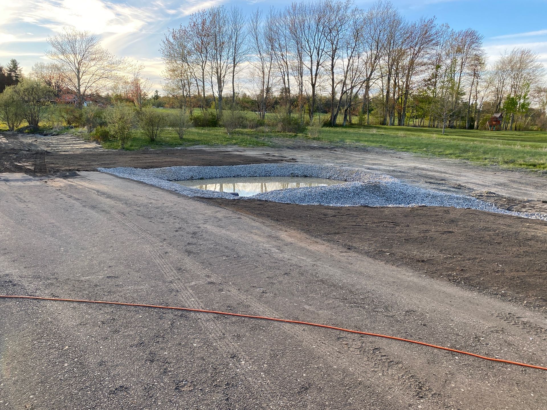 A large puddle in the middle of a dirt field with trees in the background