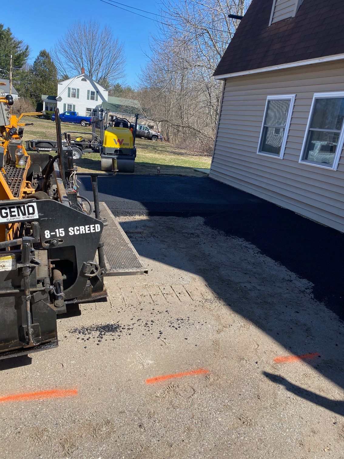 A row of asphalt paving machines are parked in front of a house