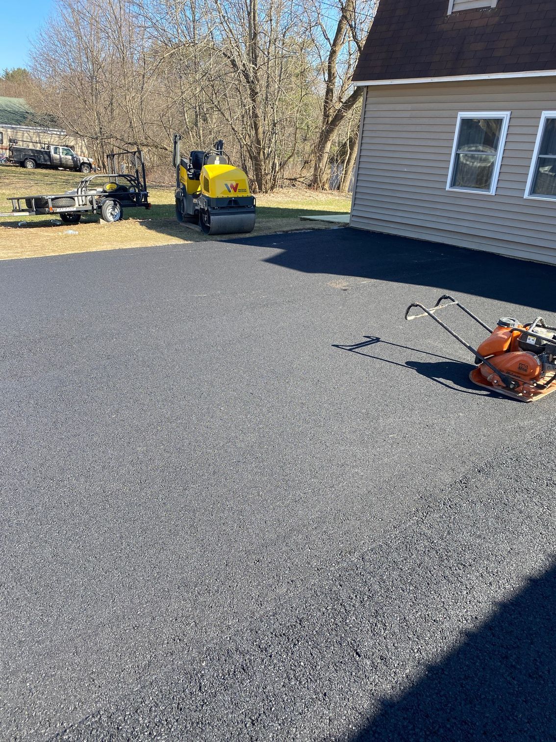 A yellow roller is sitting in a driveway next to a house