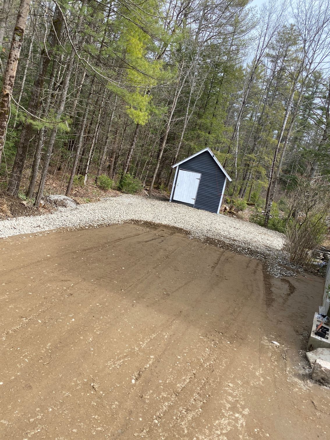 A small shed is sitting in the middle of a dirt field in the middle of a forest