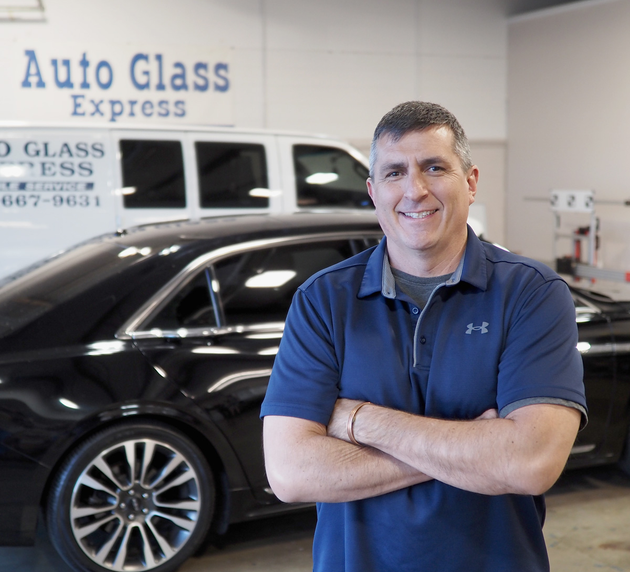 Man standing with arms crossed in an auto glass shop beside a black car