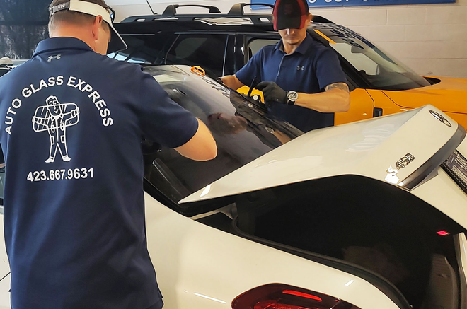 Two mechanics working on a car in a garage, one wearing a navy Auto Glass Express shirt