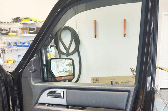 Open car door showing a side mirror and garage wall with tools and shelves.