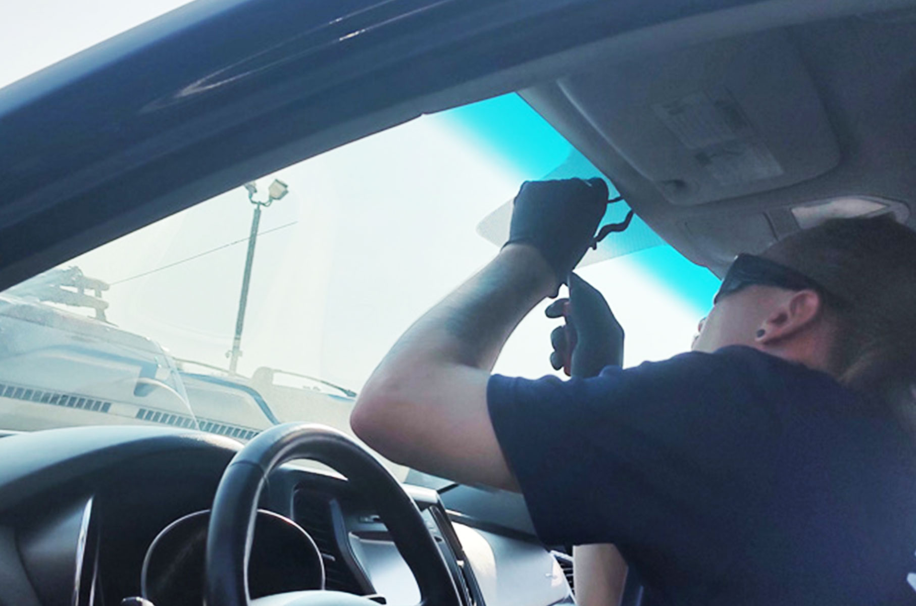 Driver adjusting a rearview mirror inside a car on a sunny day