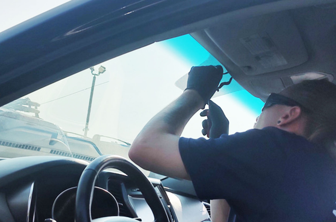 Driver adjusting a rearview mirror inside a car on a sunny day