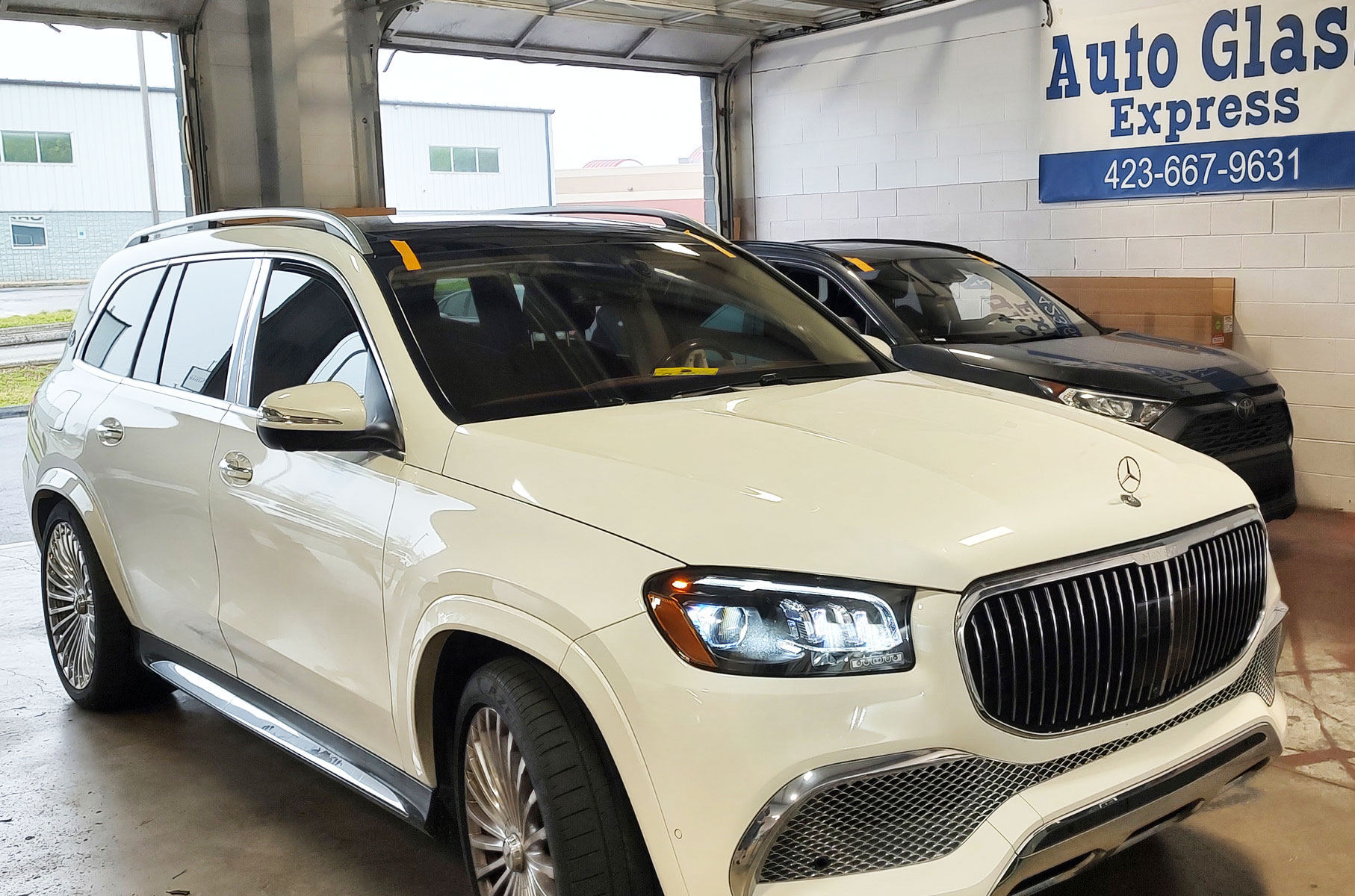 White SUV inside auto glass shop with windshield signs and repair equipment in the background