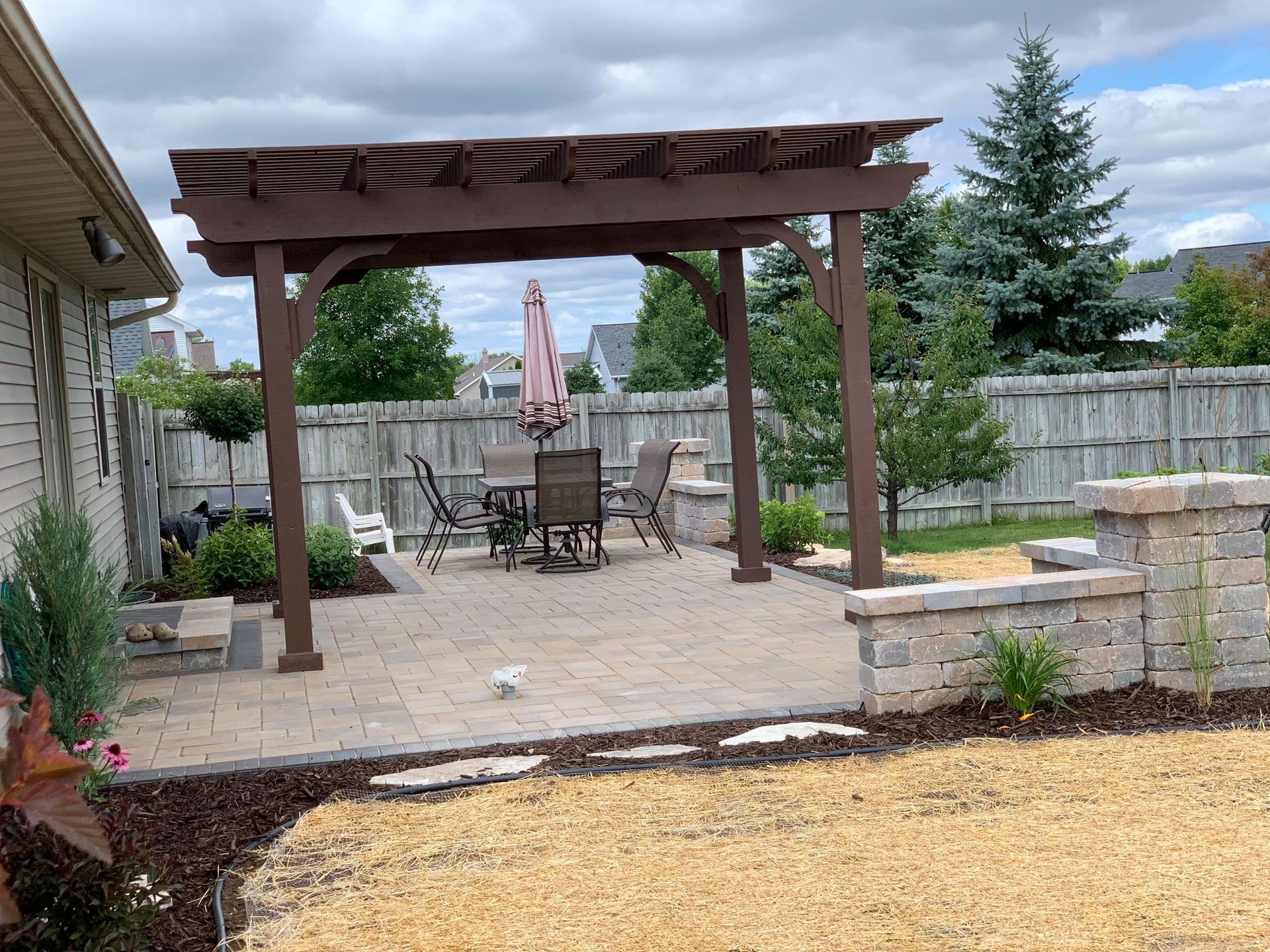 There is a pergola in the backyard with a table and chairs underneath it.