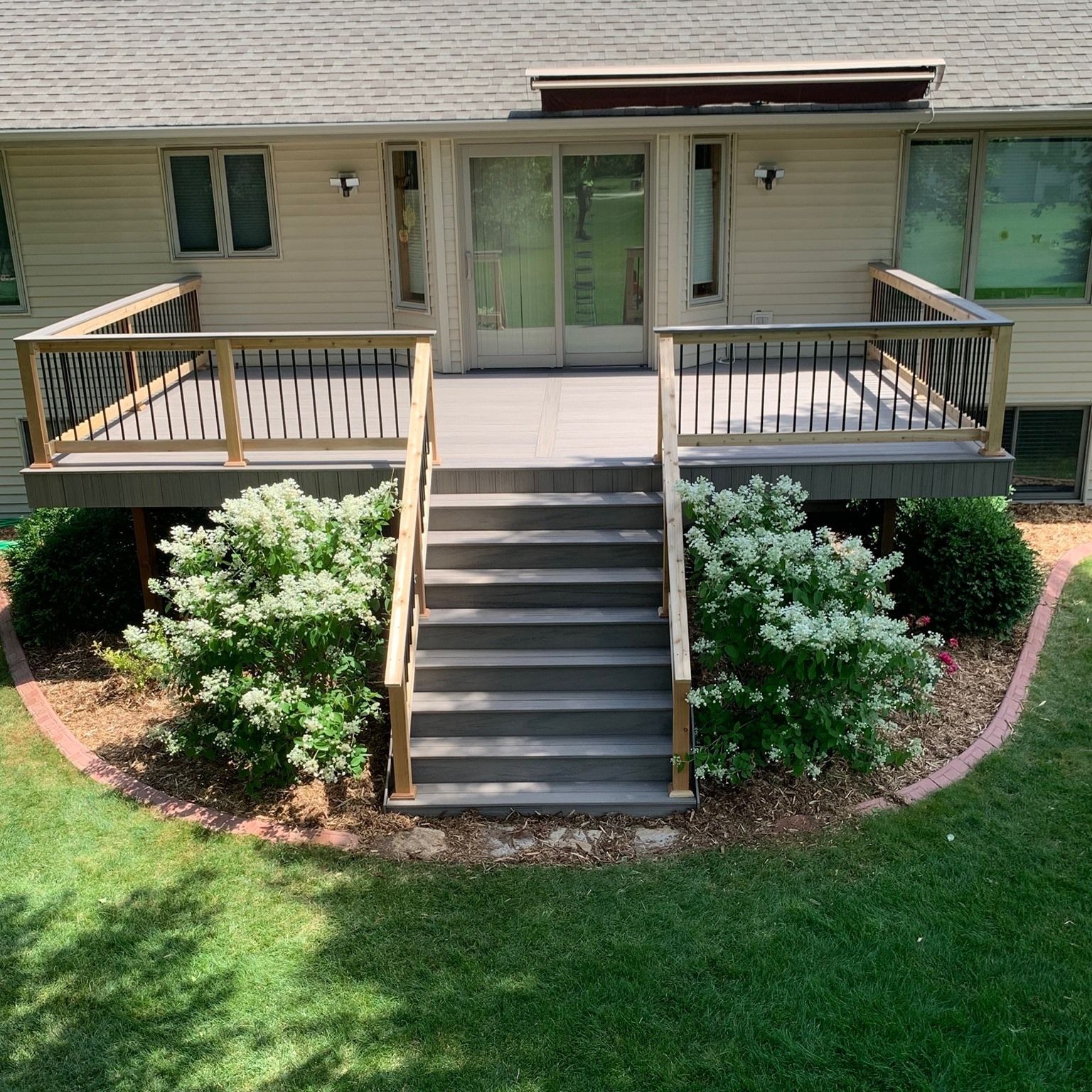 A large deck with stairs leading up to it is in the backyard of a house.