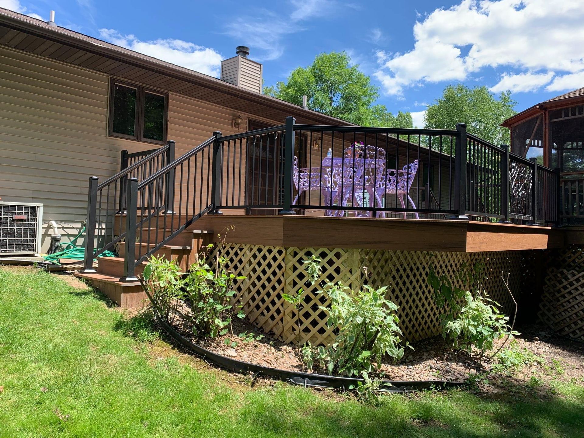 A wooden deck with a black railing is in the backyard of a house.