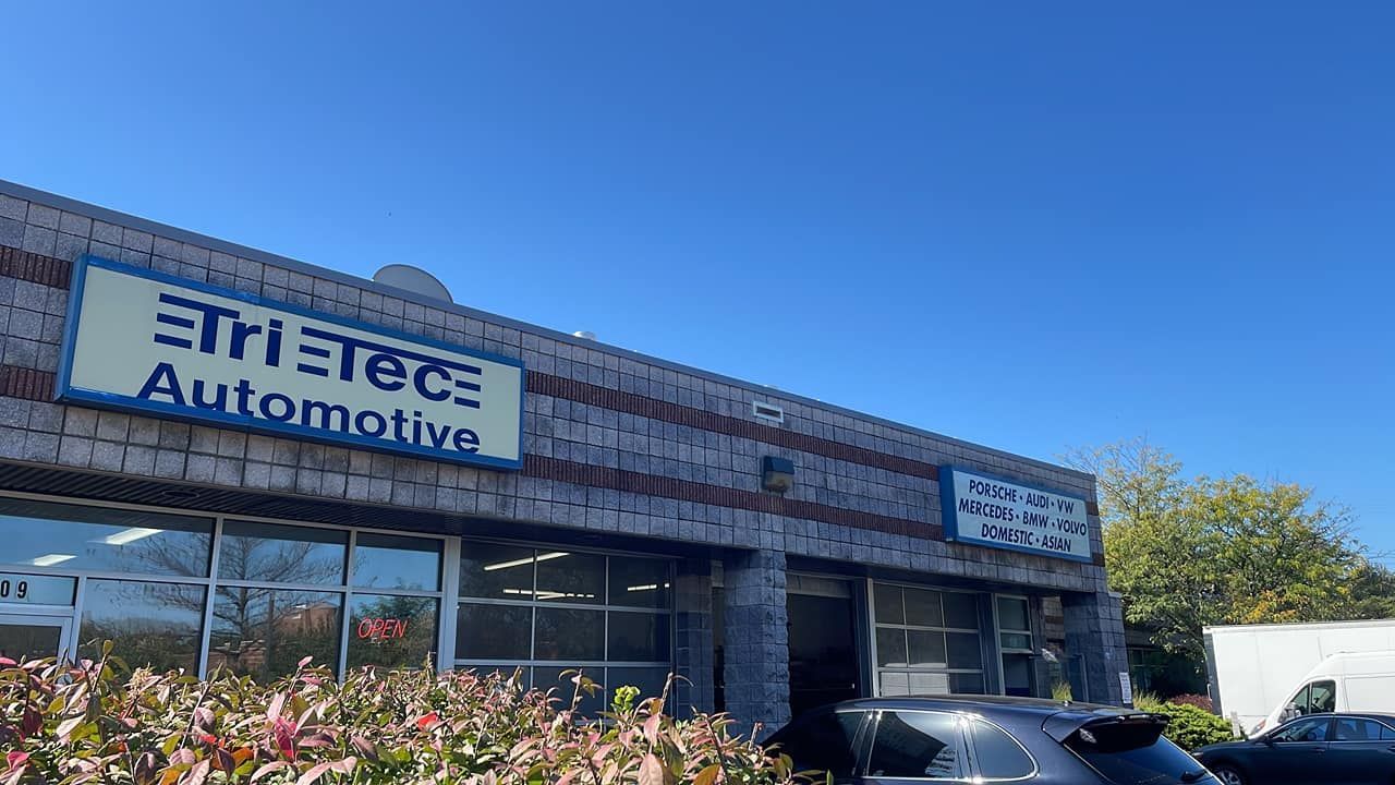 Tri-Tech Automotive building with blue sign, brick exterior, and parked cars under a clear sky.