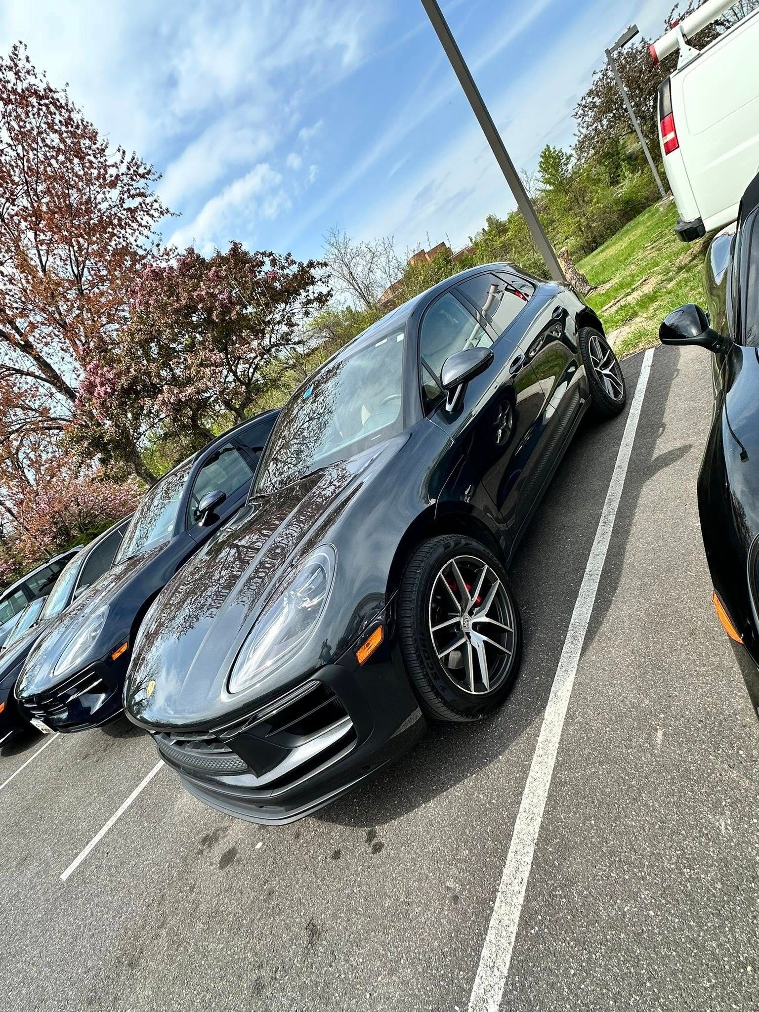 Black Porsche Macan parked in a lot on a sunny day with trees in the background.