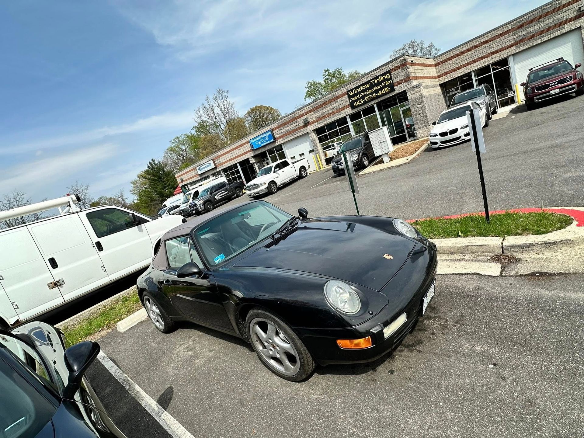 Black Porsche 911 parked in front of a strip mall on a sunny day.