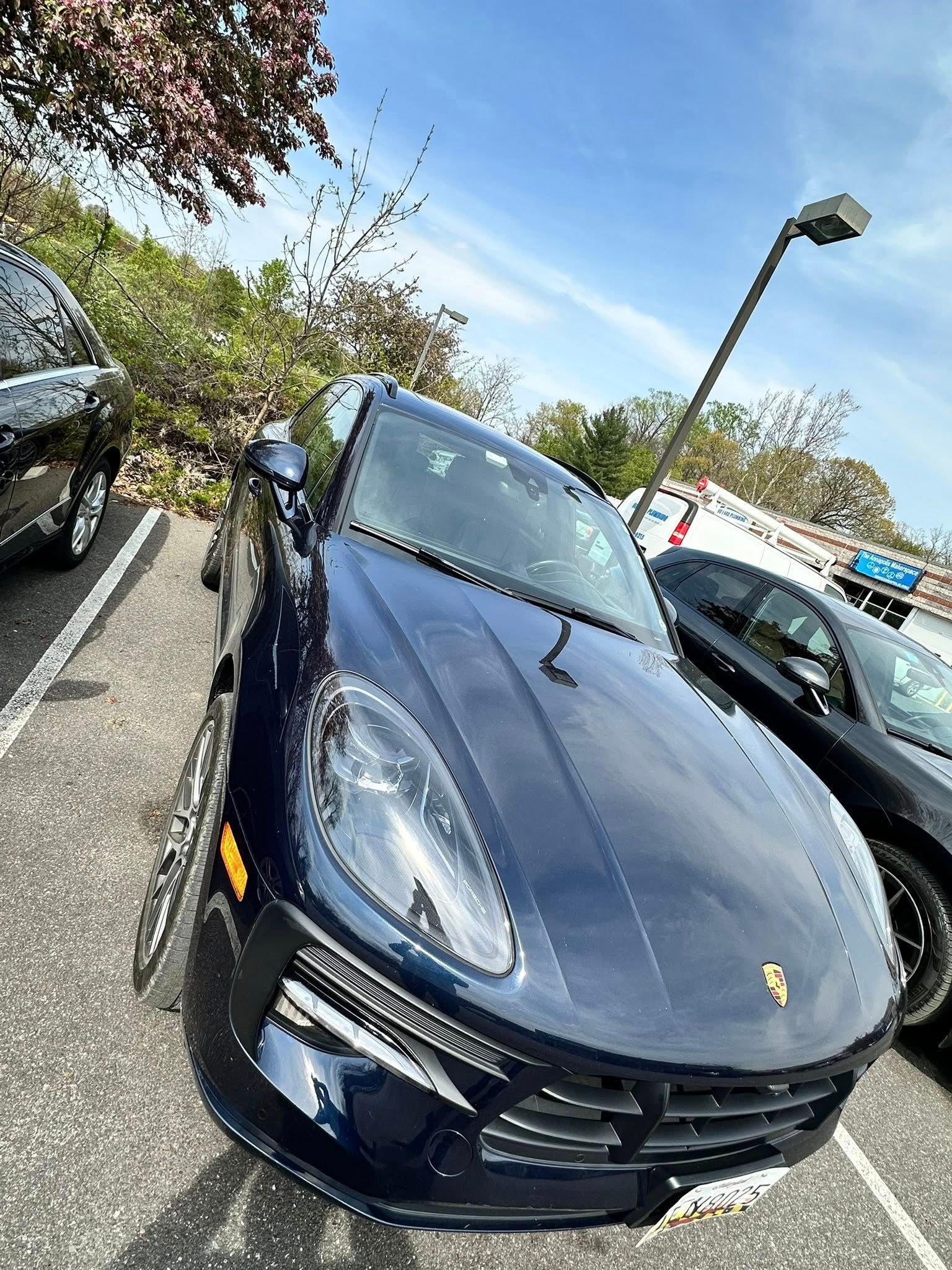 Blue Porsche Macan SUV parked in a parking lot on a sunny day.