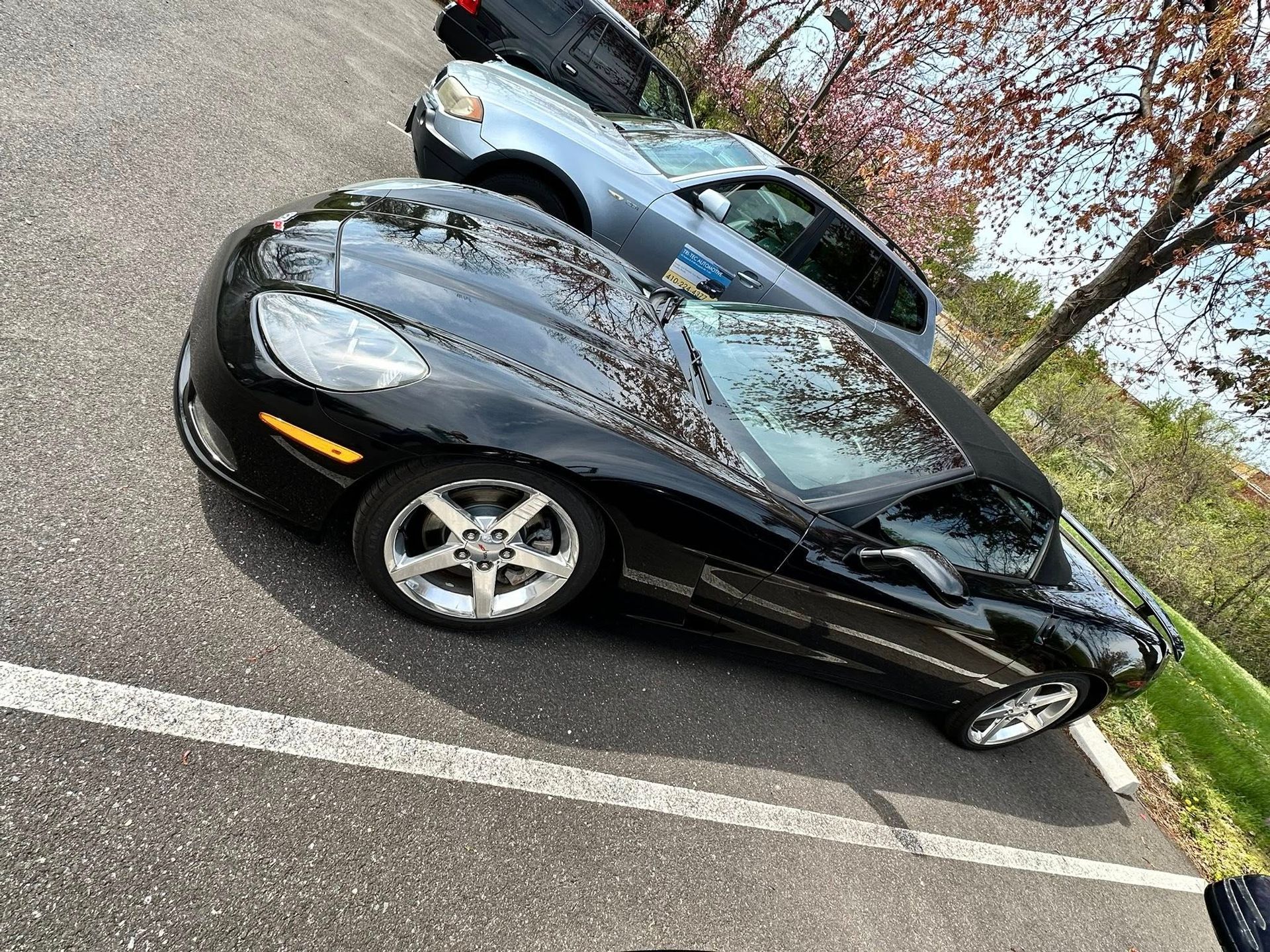 Black Corvette parked next to a light blue SUV in a parking lot.