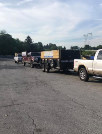 A line of pickup trucks with trailers parked on a paved lot under a clear, bright sky.