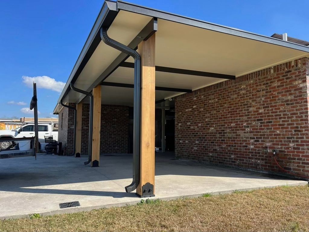 Carport with brick wall, wooden columns, and black gutters under a blue sky.