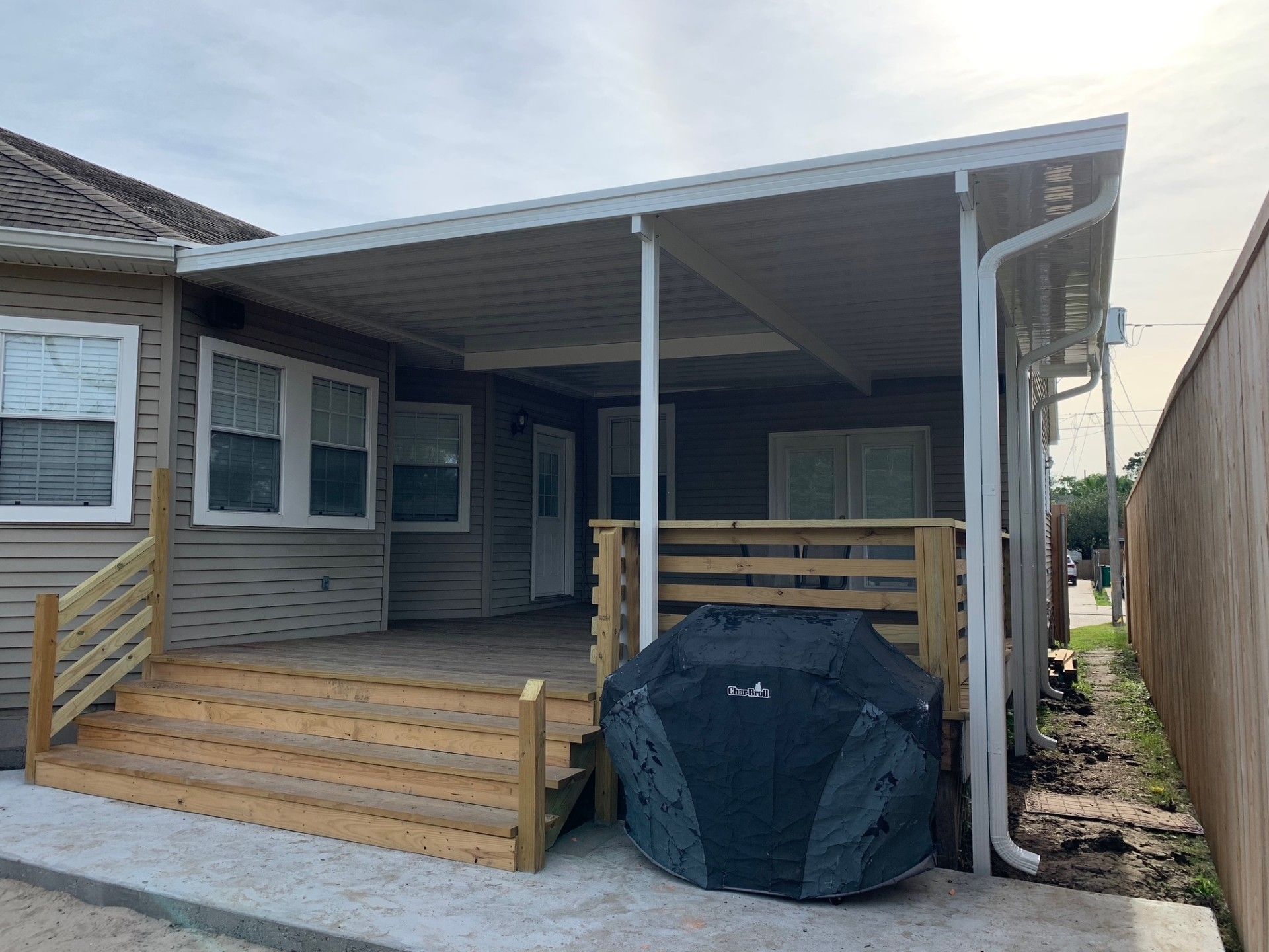 Wooden deck with a covered patio attached to a beige house, a grill is on the deck.
