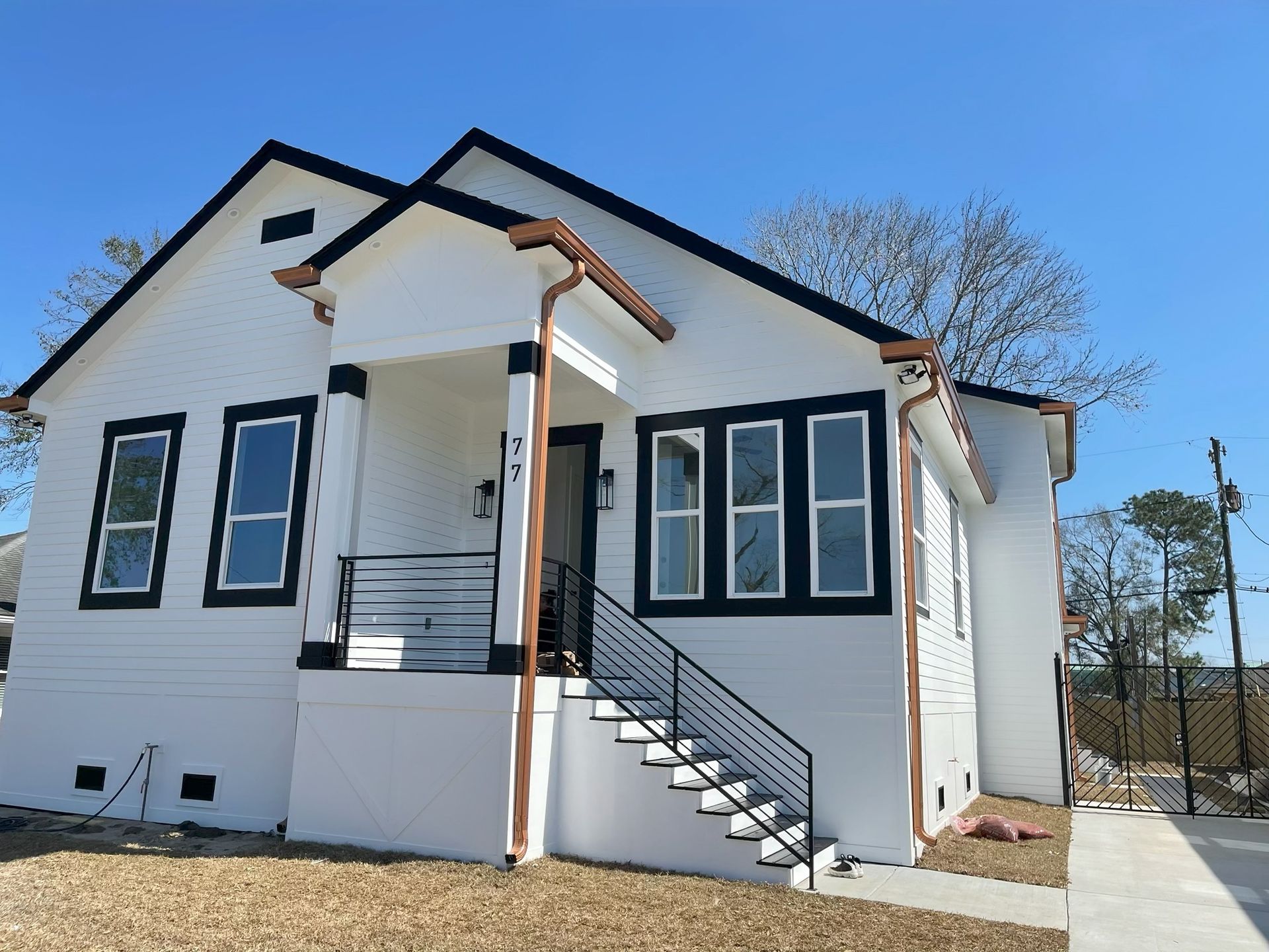 White house with black trim, copper gutters, and stairs leading to a covered porch under a blue sky.