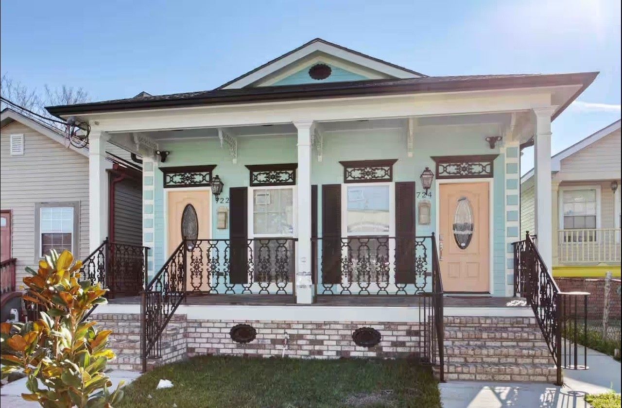 A light blue and white duplex with pastel pink doors and black shutters and railings.
