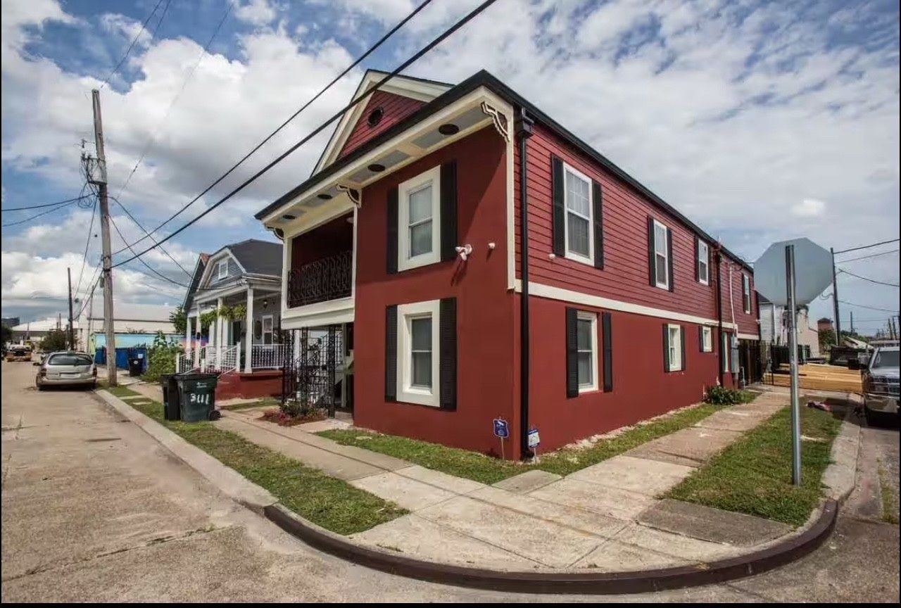 Red multi-story building on a corner lot, black trim, with a blue and white house next to it.