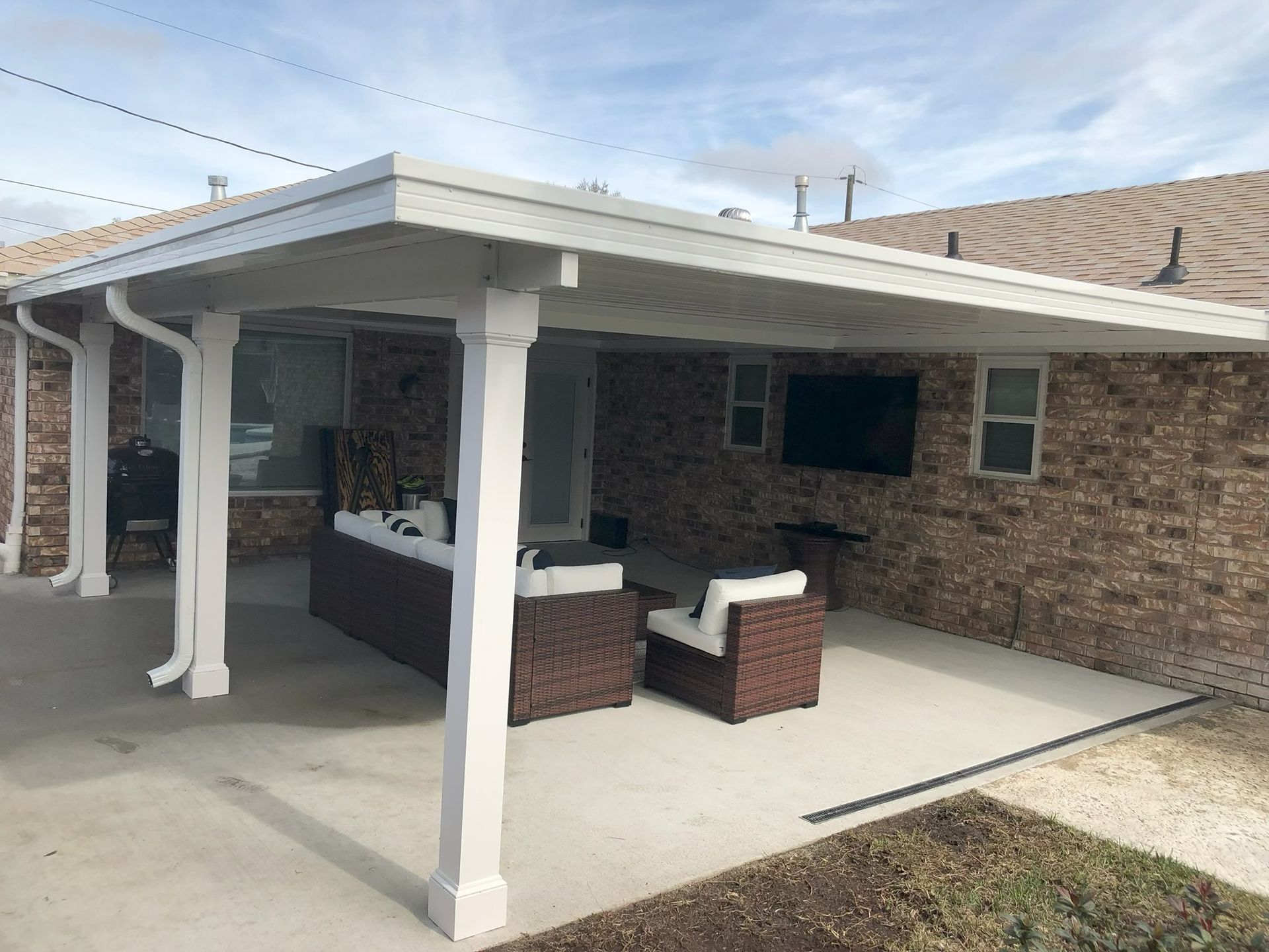 Patio with white columns, concrete floor, brick wall, and outdoor seating under a covered roof.