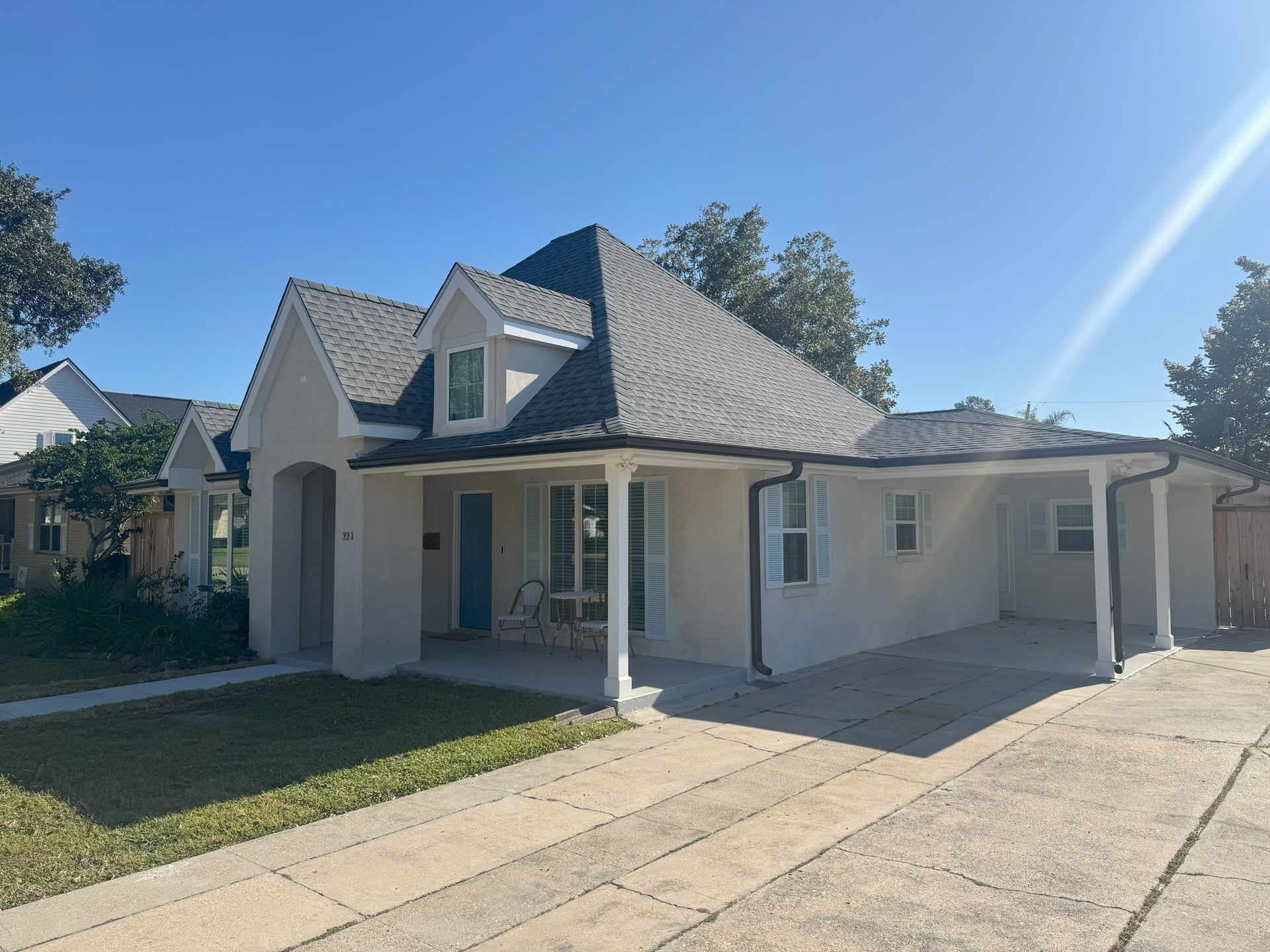 Tan house with black roof and a carport, on a sunny day.