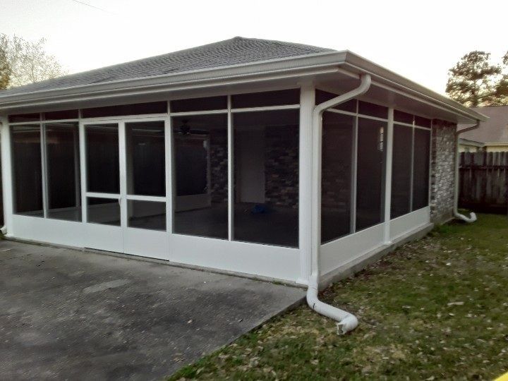 White screened-in patio attached to a brick house with a gray roof. Gutters and a concrete floor.