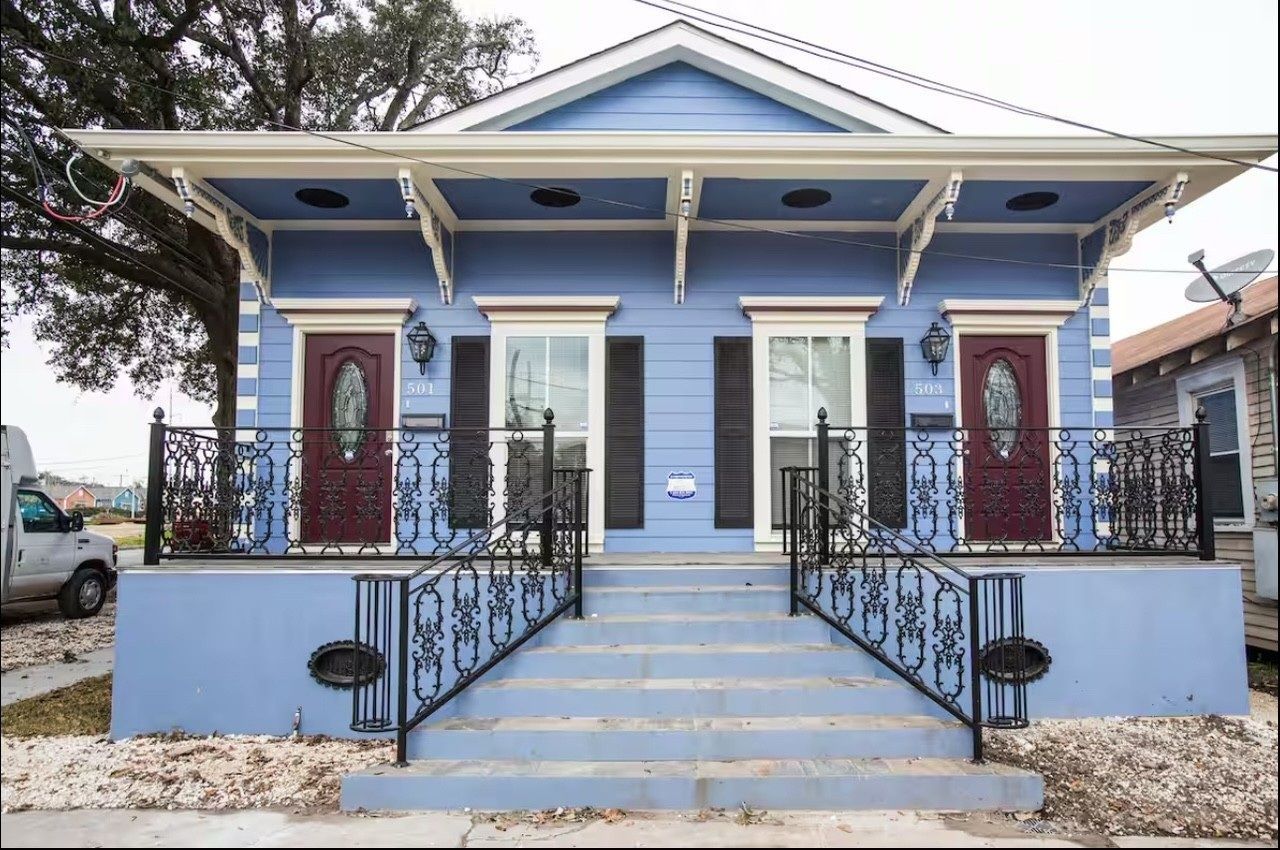Blue double house with ornate railings, maroon doors, and decorative brackets.