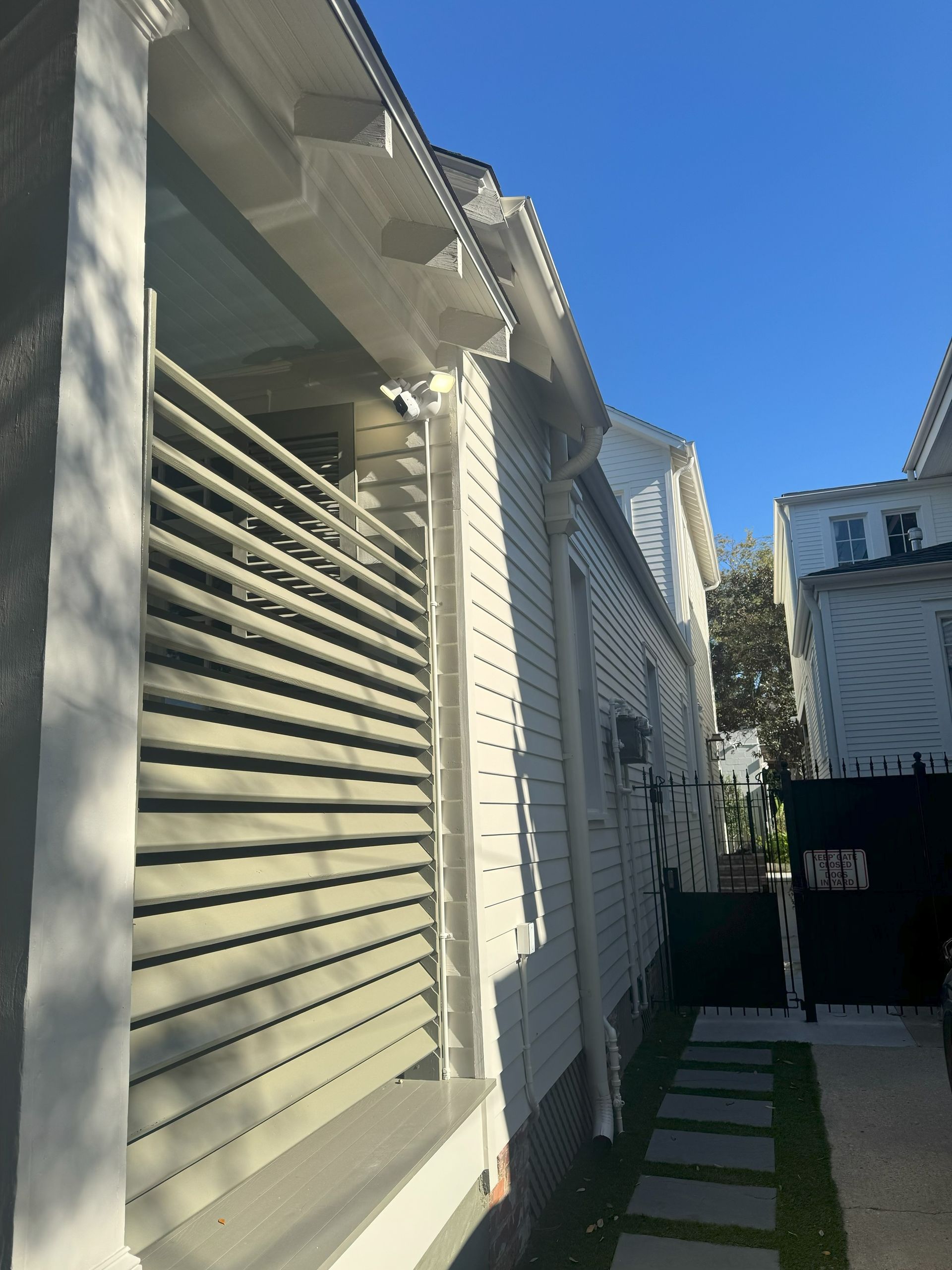 Side view of a white house with a slatted porch and a stone pathway. Clear blue sky.