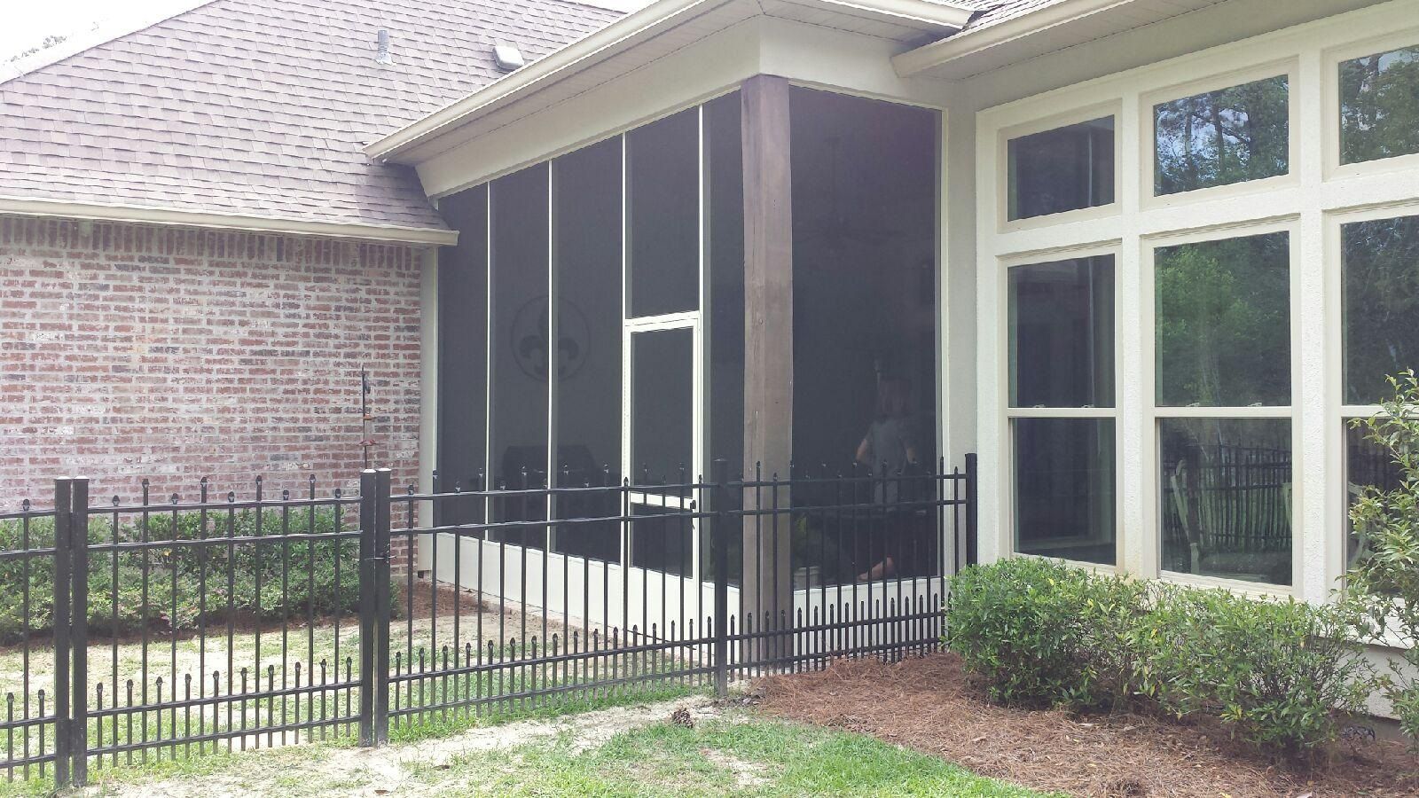 Screened porch attached to a brick house, next to a window. Black metal fence in front.